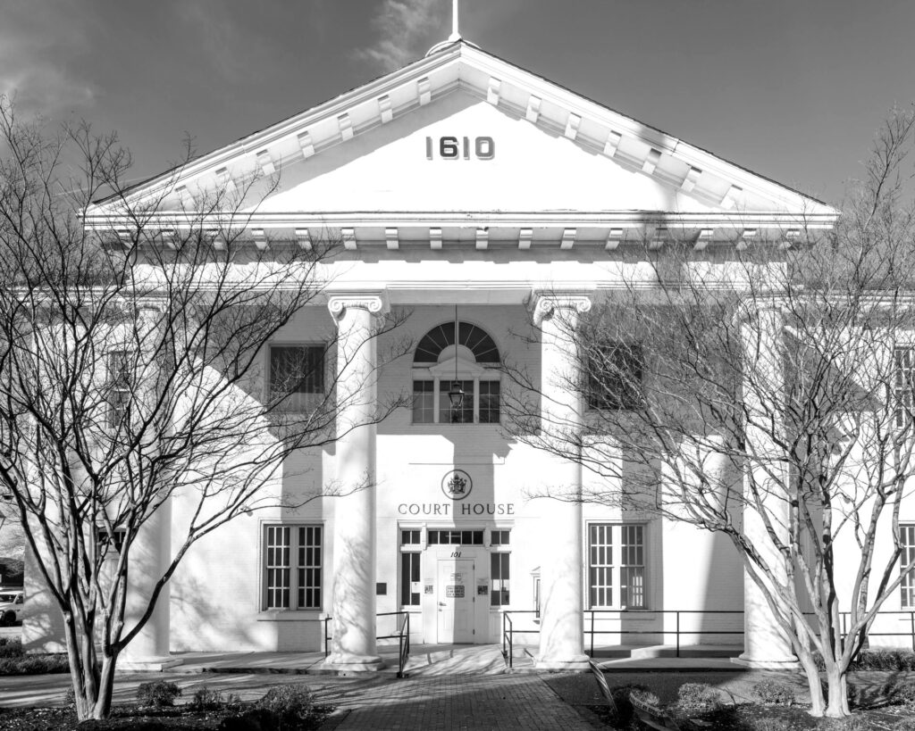 Front of a white neoclassical courthouse building with columns, in black and white